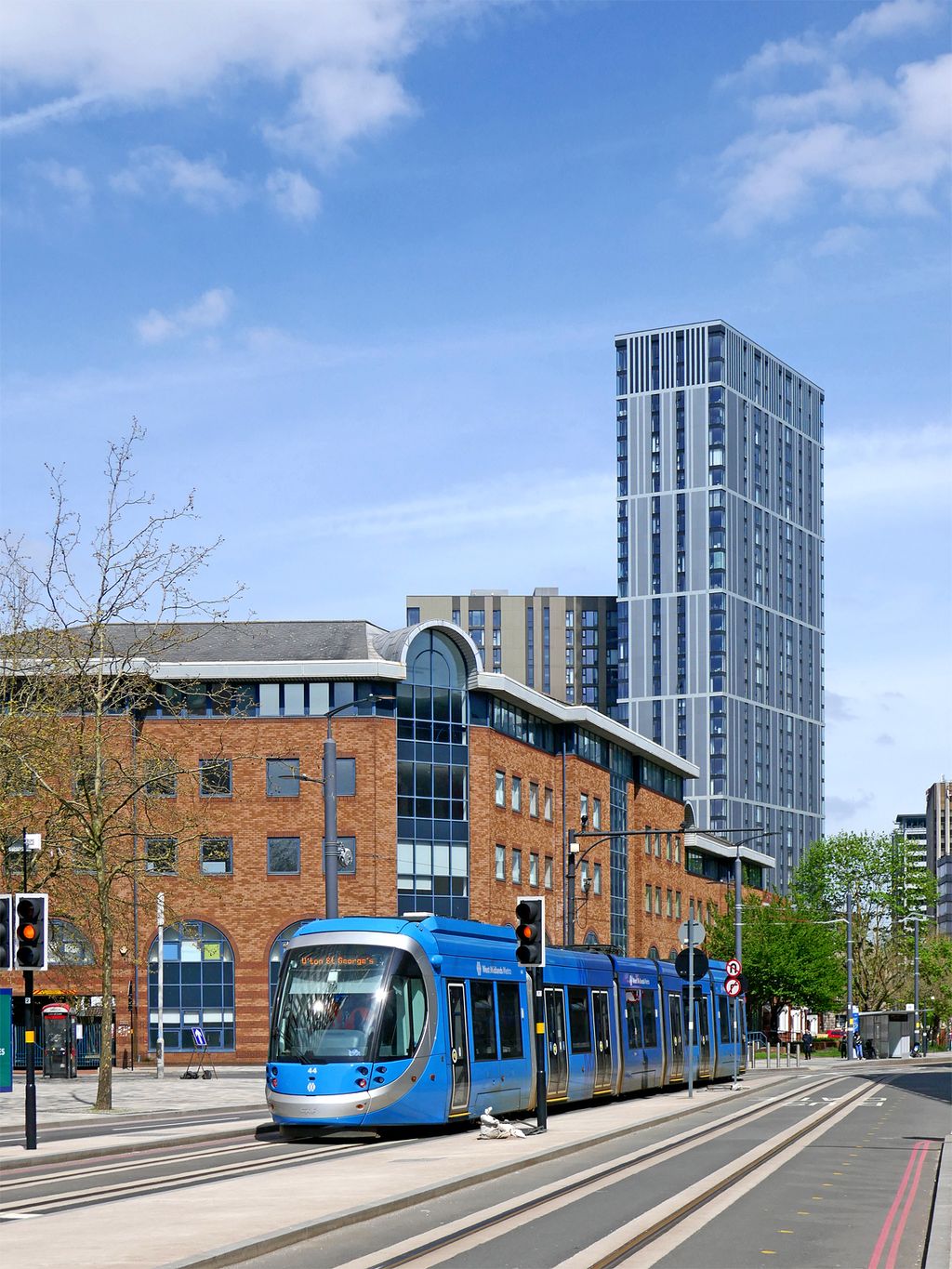 A modern tram running along a city street lined with bars and offices.