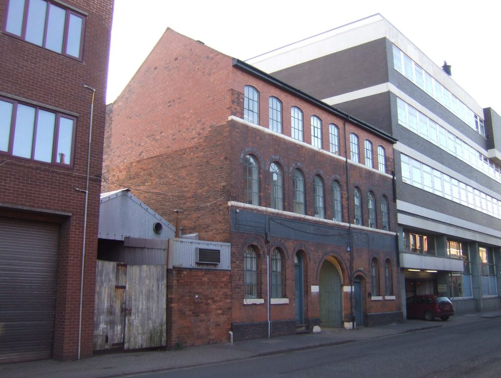 A row of brick workshop buildings with many windows along a street.