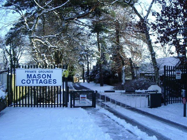 Snow-covered gated entrance with a sign reading Private Grounds, Mason Cottages, and bungalows among trees beyond.
