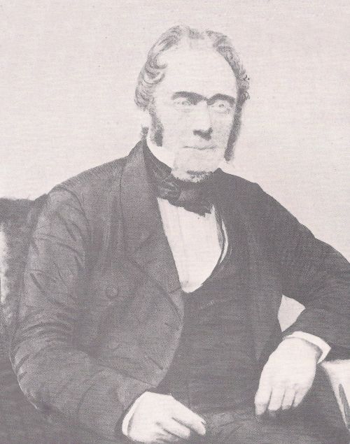 Black-and-white portrait of a seated middle-aged man in a dark Victorian coat.