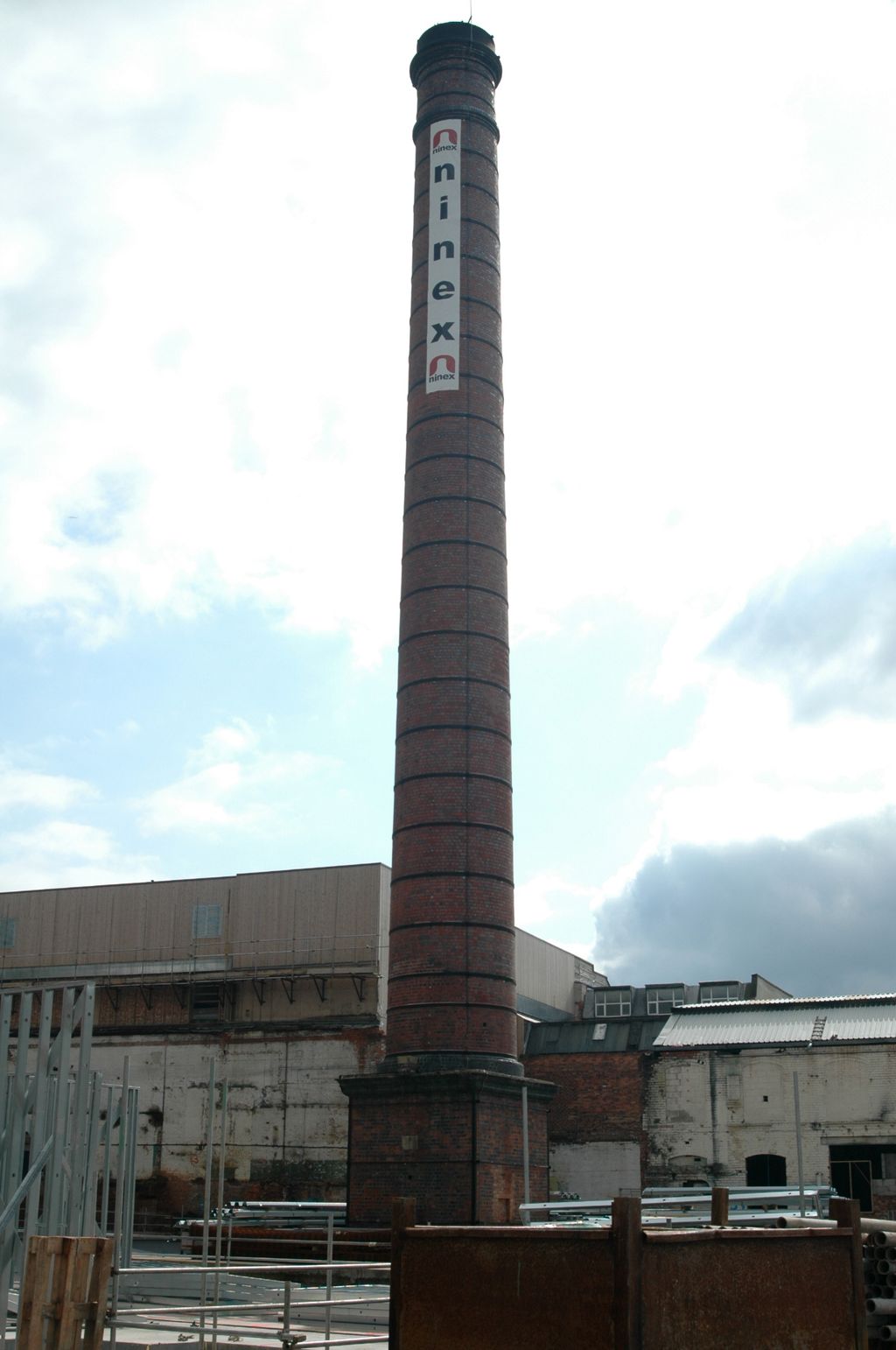 Tall square-section brick chimney rising above industrial buildings.