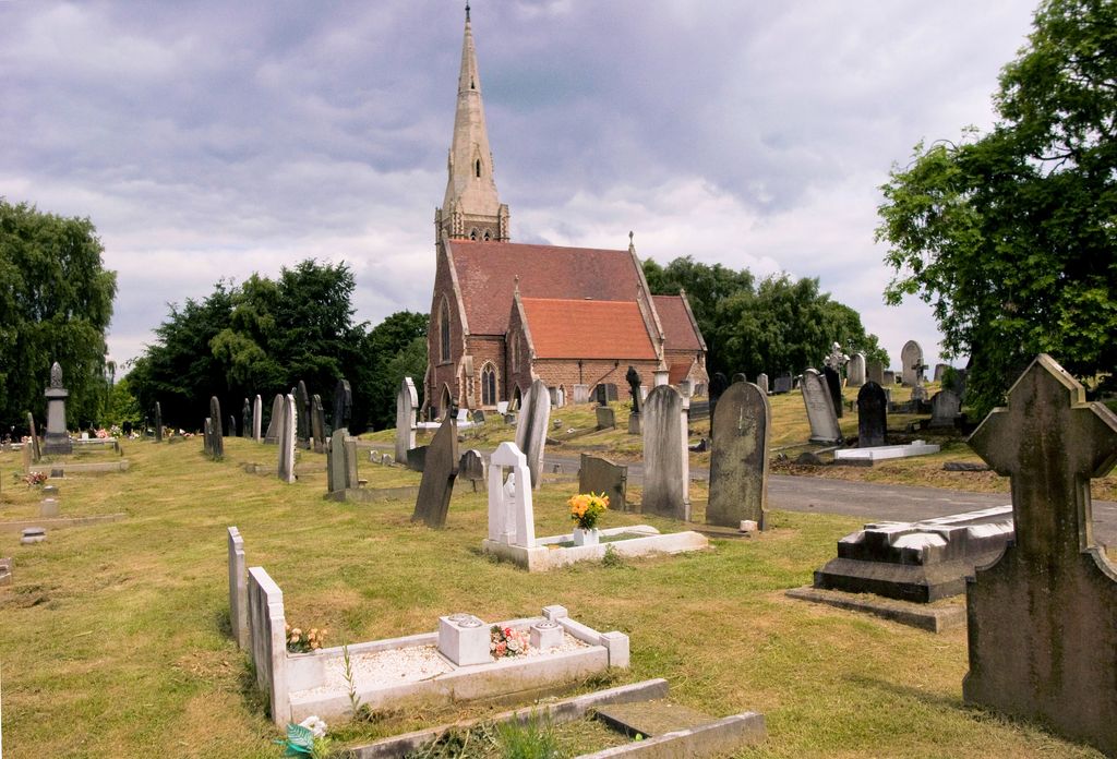 A Gothic stone chapel with a spire among trees and gravestones.