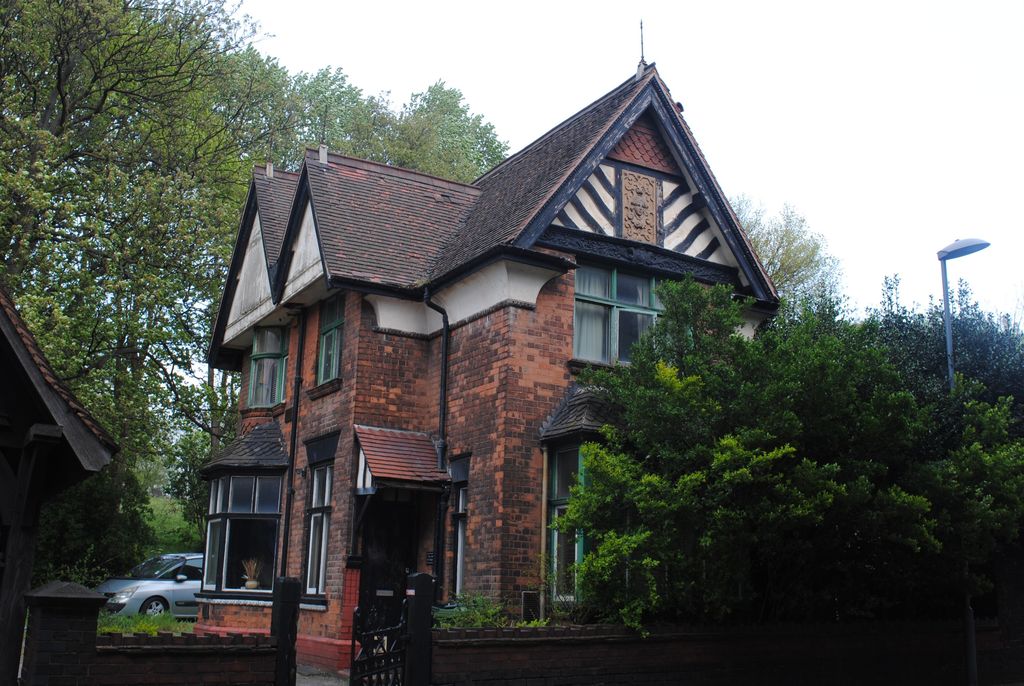 A red-brick lodge with half-timbered gables behind a hedge.
