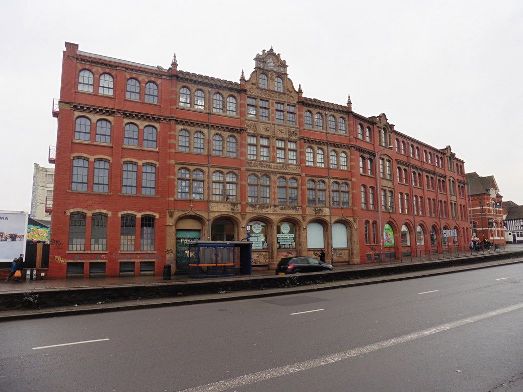 A long four-storey red-brick and terracotta factory front beside a main road.