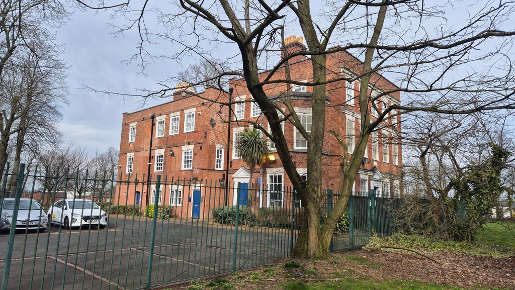 A plain red-brick Georgian house seen through bare trees and railings.