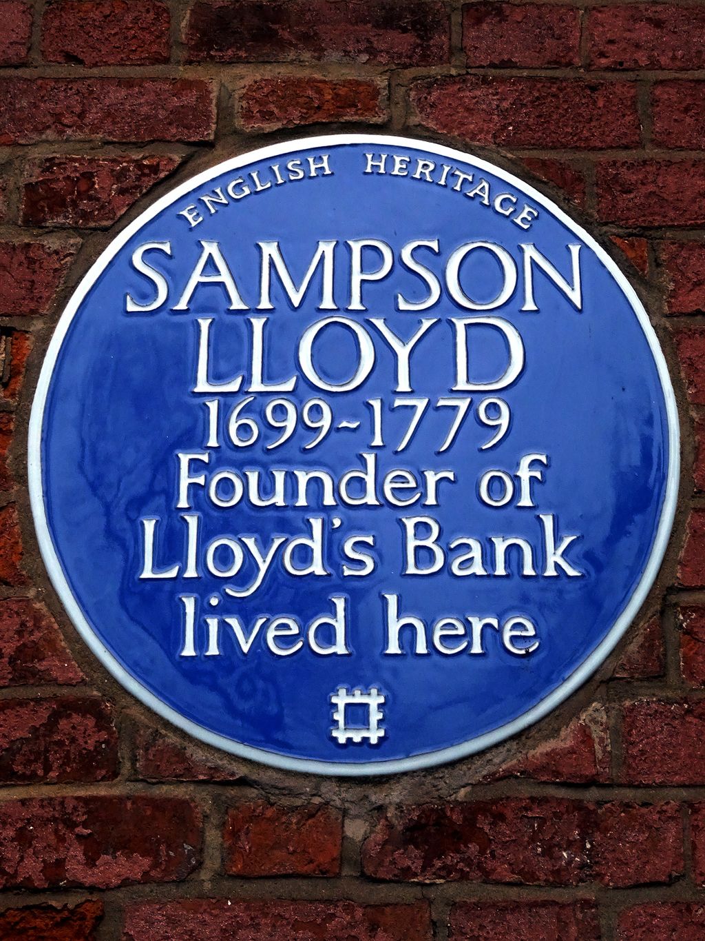 A round blue English Heritage plaque on a brick wall.