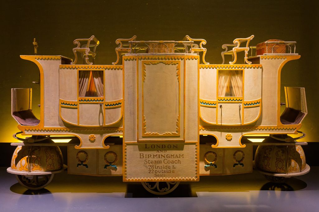 A cream and gold model of a long steam coach with two enclosed compartments, seats on the roof and a panel reading ‘London and Birmingham Steam Coach, 28 inside & 22 outside seats’.