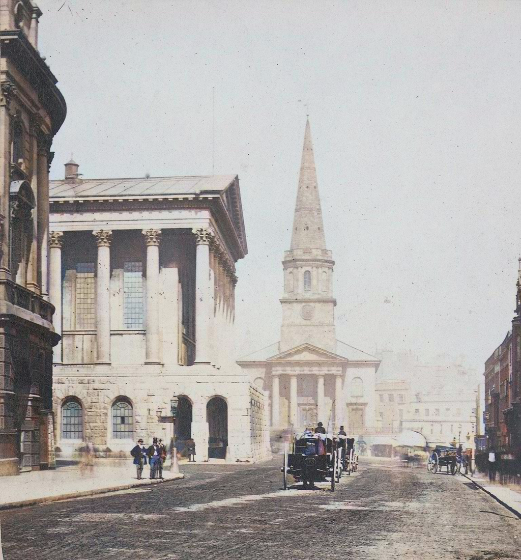 Victorian street photograph, artificially coloured, looking up a street past a columned hall to a church portico and spire.
