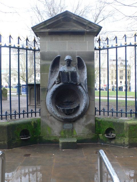 A stone drinking fountain with a carved angel holding an open book above a shell basin.