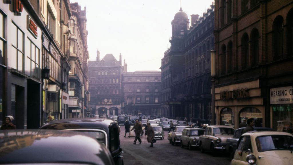 A 1960s city street with the spire of a Victorian building closing the view.