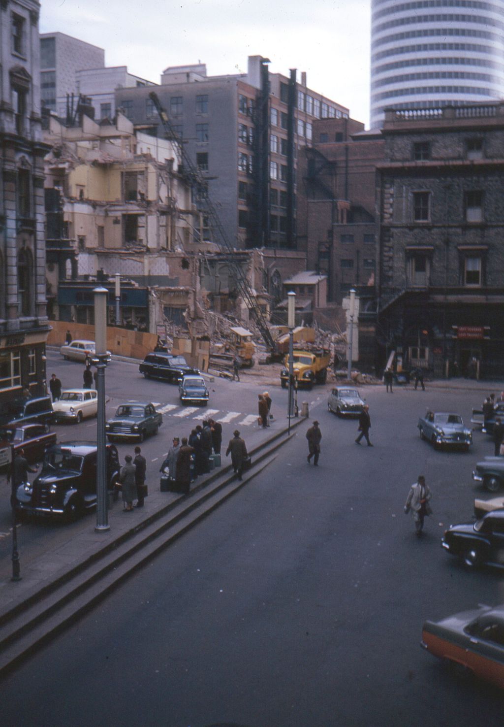 Colour photograph of a Victorian building half demolished, with taxis waiting below and a new round tower block behind.