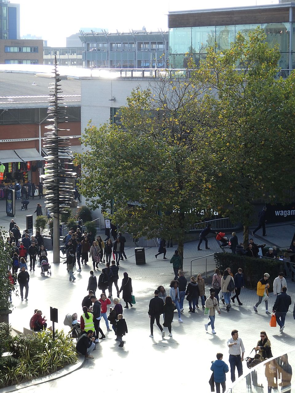 A pedestrian street in a modern shopping centre, with shoppers and glass shopfronts.