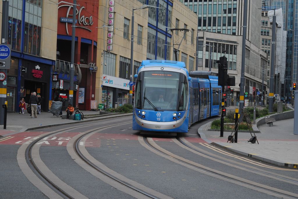 A blue tram turning a corner on a paved city street lined with shops.