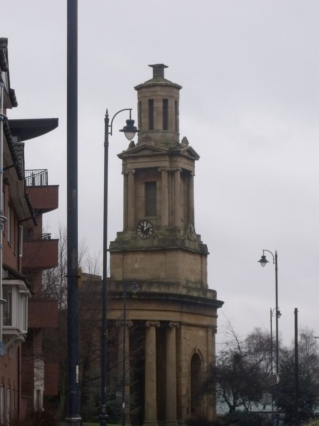 Close view of a classical stone church tower with a clock, above curved Ionic columns.
