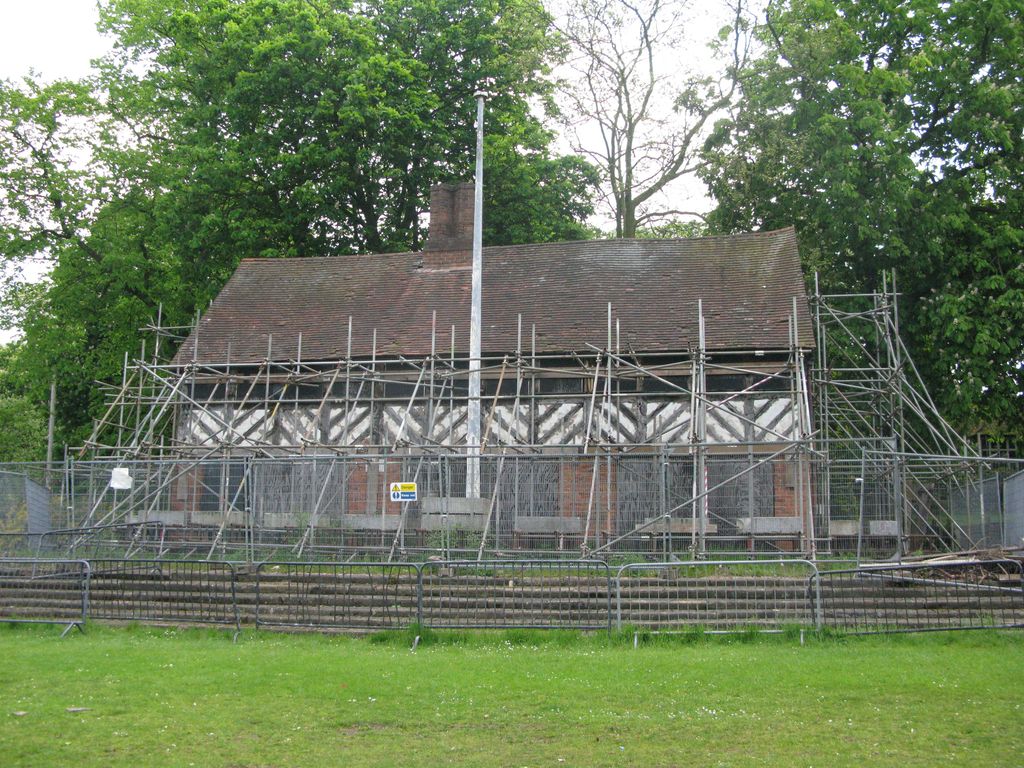A black-and-white timber-framed building with three gables and a brick ground floor in a park.