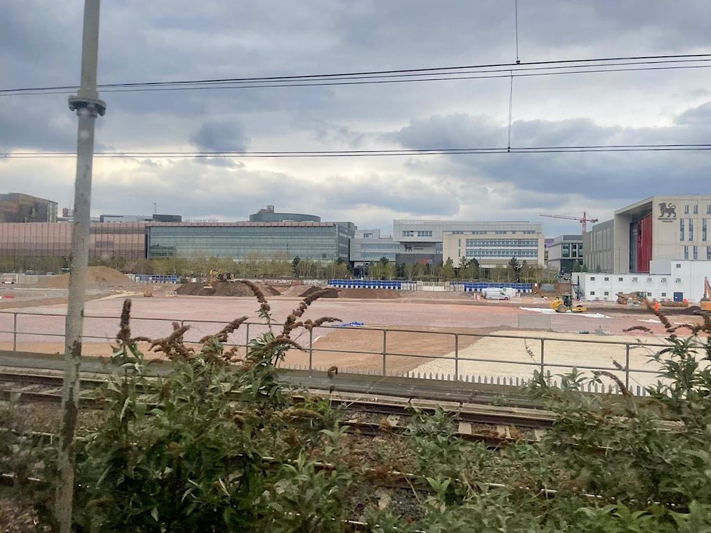 A large cleared construction site with cranes and city buildings beyond.
