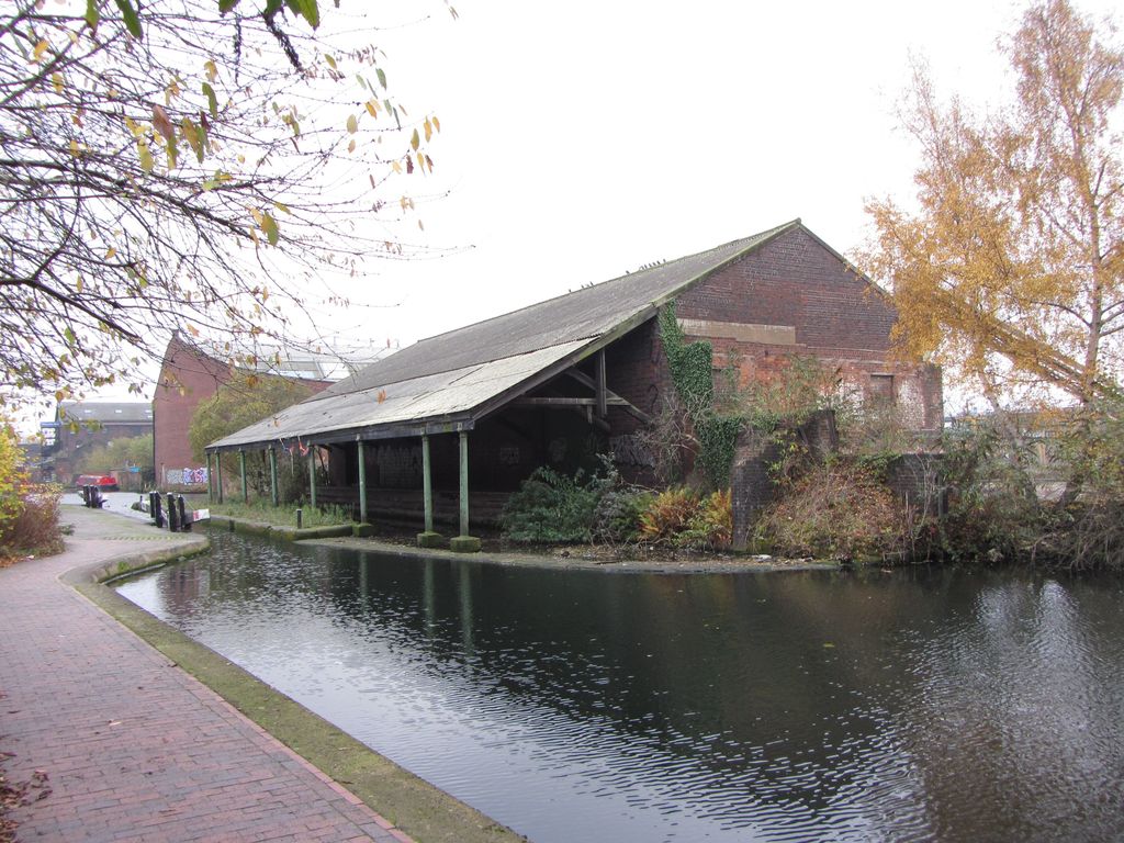 A single-storey brick warehouse with a long overhanging roof beside a canal.