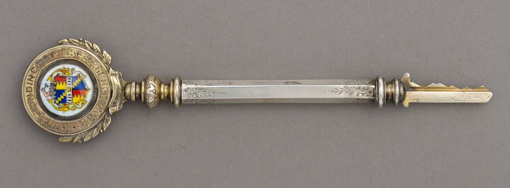 Ornate silver ceremonial key with an enamelled Birmingham coat of arms in a laurel-wreath bow, photographed on a grey background