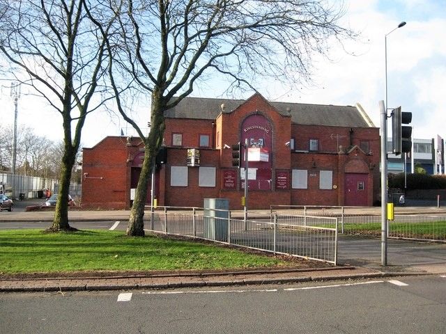 Large 1930s red-brick pub with a tall central gable and boarded windows behind railings on Kingstanding Circle, January 2018