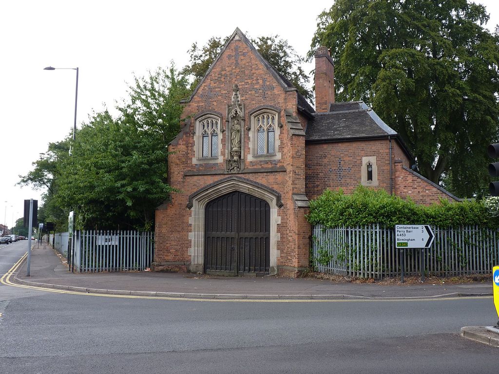 Gothic Revival brick gatehouse with a carved stone arch, niche statue and tall chimney at the junction of Chester Road and College Road