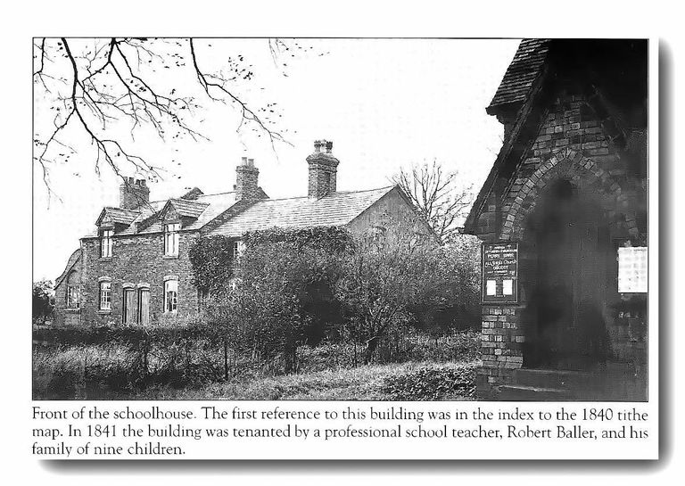 An old ivy-covered brick schoolhouse with dormers and tall chimneys behind a hedge, with a church noticeboard in a brick porch at right