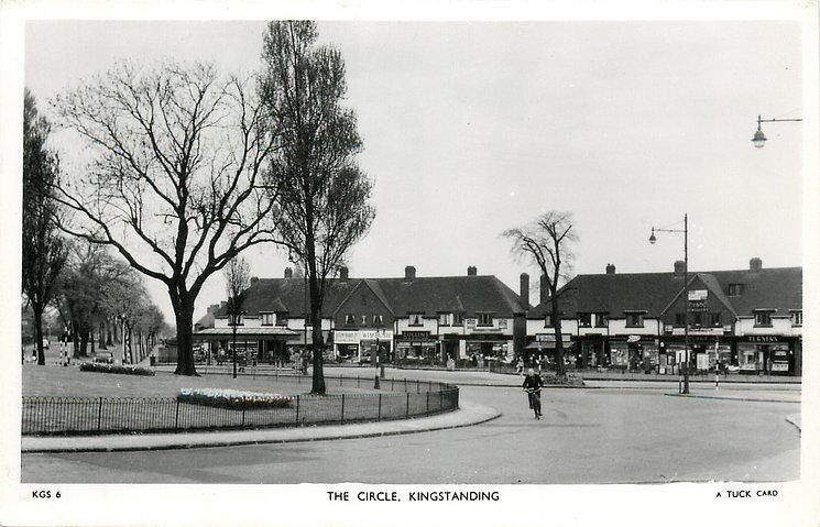 Black-and-white postcard of the Circle, Kingstanding, around 1950: a parade of shops behind the railed garden in the middle of the Circle, with a cyclist on the road